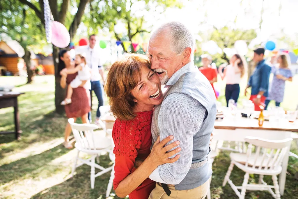 A senior couple happily dancing and laughing at a big party celebration symbolizing how ai hearing aids help with speech clarity even in challenging listening environments.